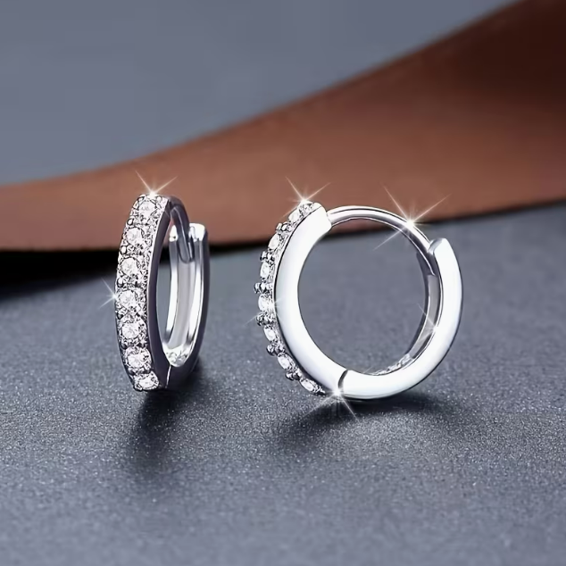 Lumière Pavé Huggie Hoop Earrings – silver huggie hoops resting on wooden surface with white rose