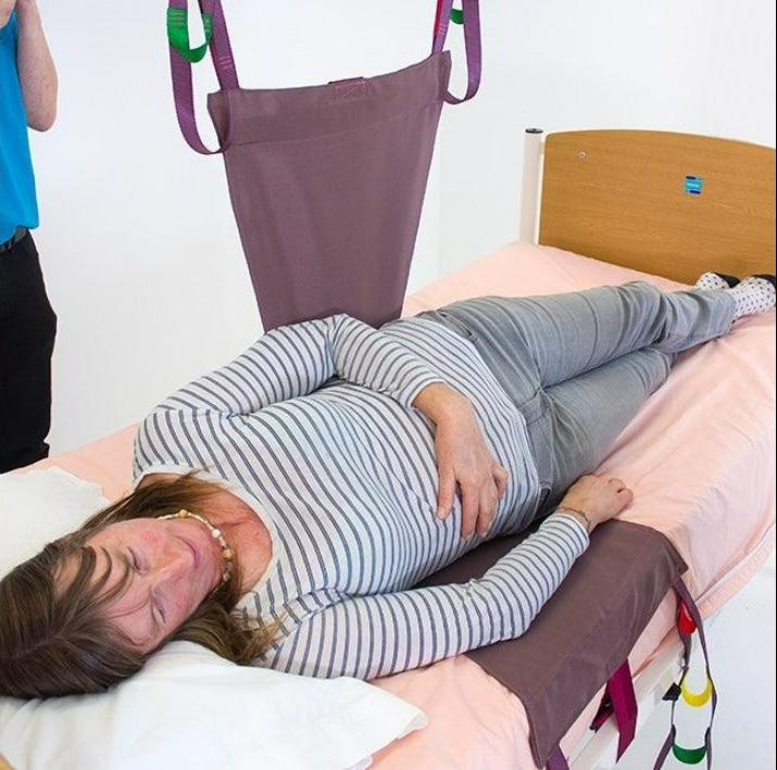 Nurse assisting elderly patient to stand using transfer aid and wheelchair