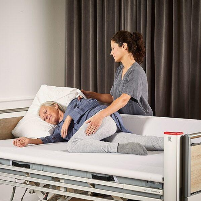 Caregiver turning patient using slide sheet on care bed