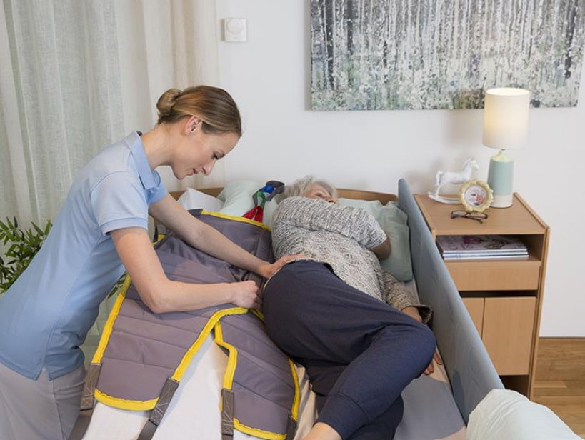 Caregiver using patient turning sheet to reposition elderly woman on hospital bed